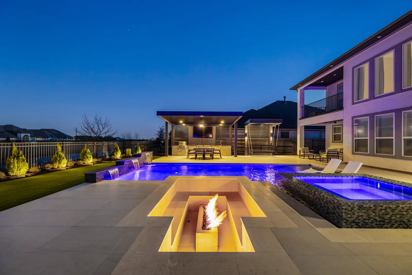 Lit fire pit by the pool at dusk, with aluminum covered patios in the background.